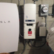 Rhonda "Honey" Phillips poses next to a Tesla Powerwall battery and inverter connected to a solar panel array in her yard in Middletown Springs